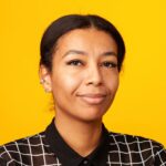 Close up studio portrait of a cheerful middle aged african american woman in a plaid blouse against a yellow background